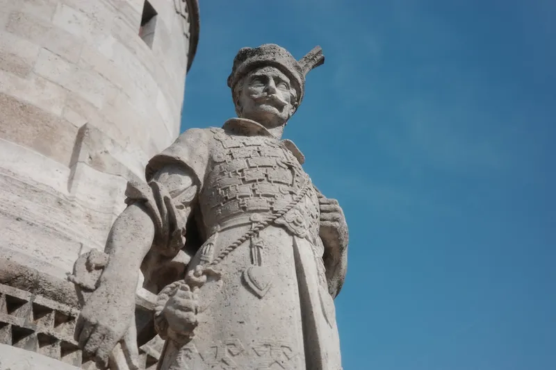 Statue of a man wearing armor, against a blue sky.